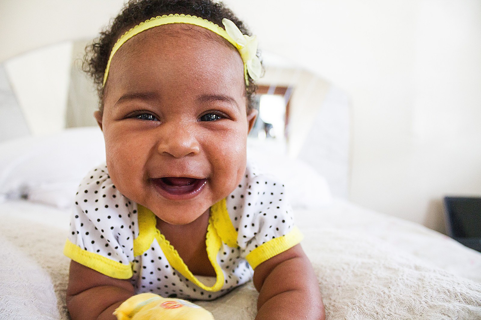 A smiling African American baby wearing a yellow headband, all smiles during a therapy play session.